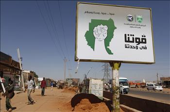 سودانيون يسيرون قرب لافتة كتب عليها «قوتنا في وحدتنا» في الخرطوم في 11 كانون الثاني الحالي