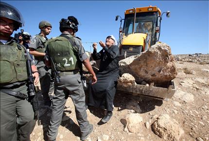 فلسطيني يحاول منع قوات الاحتلال من هدم خيم وحظائر وآبار مياه في قريتين صغيرتين في جنوبي يطا في الخليل أمس. (أ ف ب) 