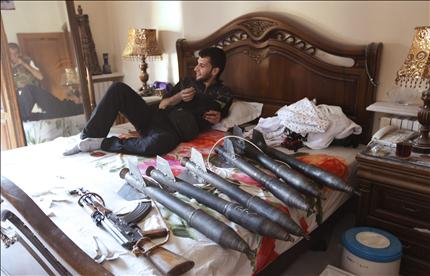 عنصر من «الجيش الحر» يرتاح على سرير وإلى جانبه صواريخ وأسلحة في حي سيف الدولة في حلب أمس (رويترز) 