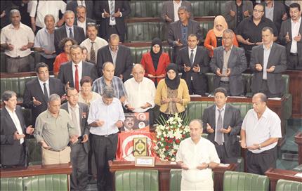نواب يقفون أمام كرسي النائب محمد البراهمي قبل بدء الجلسة في المجلس الوطني التأسيسي في تونس أمس (أ ف ب) 