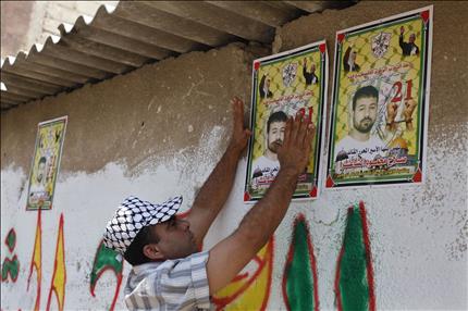 فلسطيني يعلق صوراً للأسير صلاح الشاعر قبل إطلاق سراحه في خان يونس في جنوب قطاع غزة أمس (رويترز) 