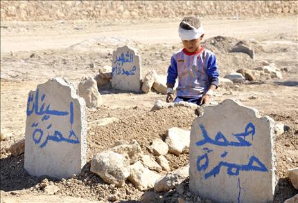 الطفل علي حمزة (ثمانية أعوام) يجلس أمام قبر أخيه محمد وأخته اسينات، اللذين قضيا في التفجير الذي استهدف مدرسة ابتدائية في قرية القبك، أمس (أ ب) 