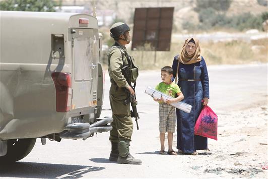 جندي اسرائيلي يوقف فلسطينية وطفلها على مدخل بلدة يطا القريبة من الخليل في الضفة الغربية المحتلة أمس (رويترز)